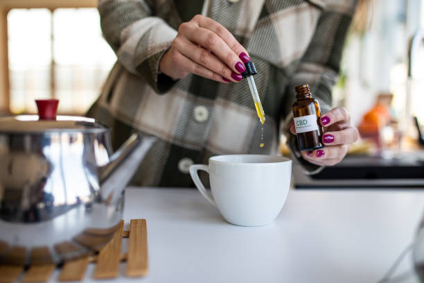 Woman adding CBD oil with a pipette into her tea to use it as a medicine.