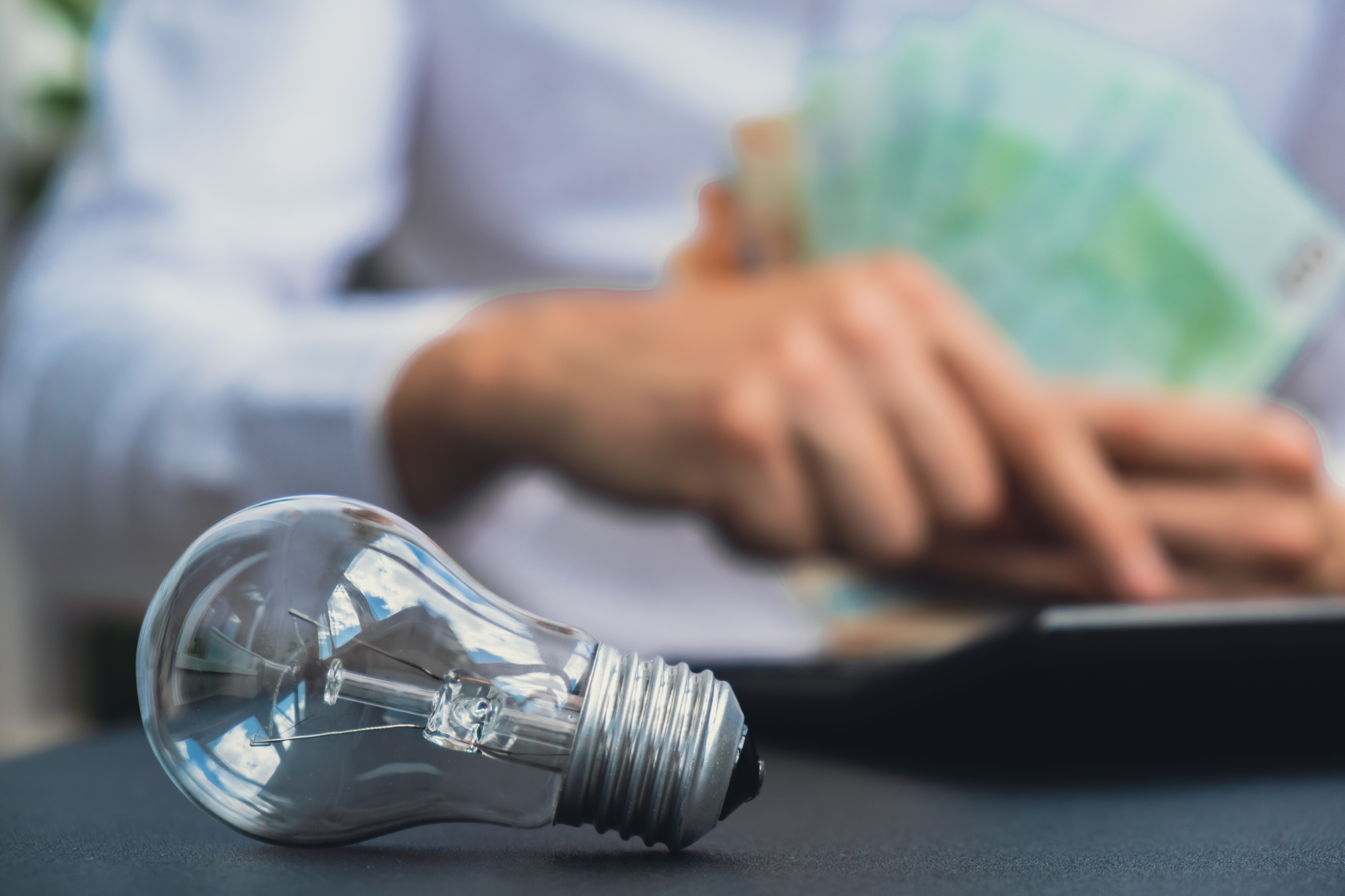 Electric light bulb. Man hands counting expenses bills on electricity banknotes of euro cash accounting on calculator. Close up of hands unrecognizable Businessman. High prices for energy. Save up budget investment concept Planning budget and estimating costs